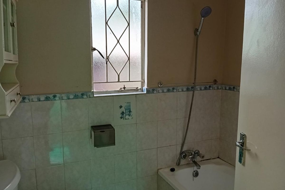A functional bathroom featuring a bathtub with a handheld shower attachment, tiled walls, and a window with security bars.