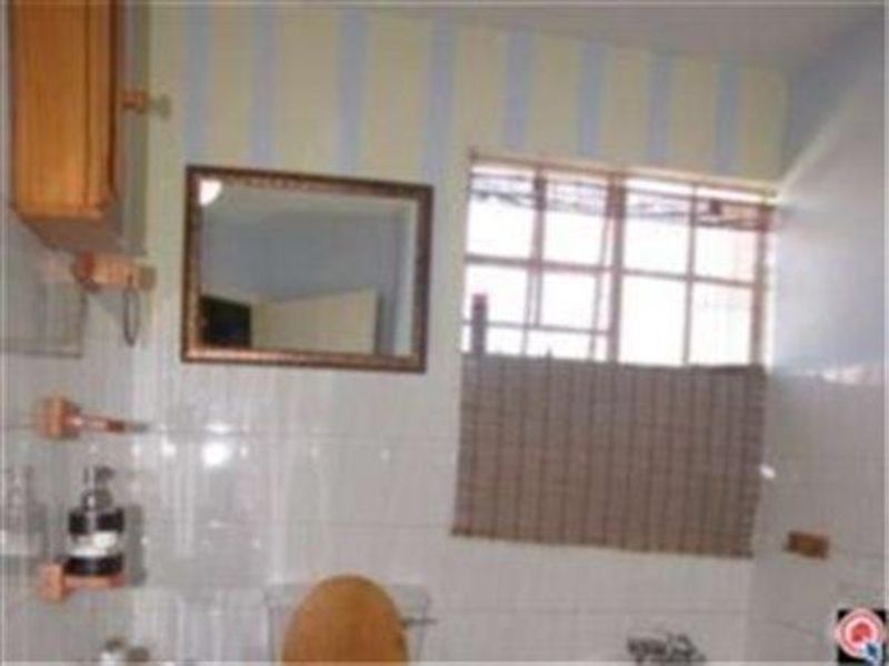 A dated bathroom featuring tiled walls, a wall-mounted mirror, and a window, offering potential for modernization and renovation.