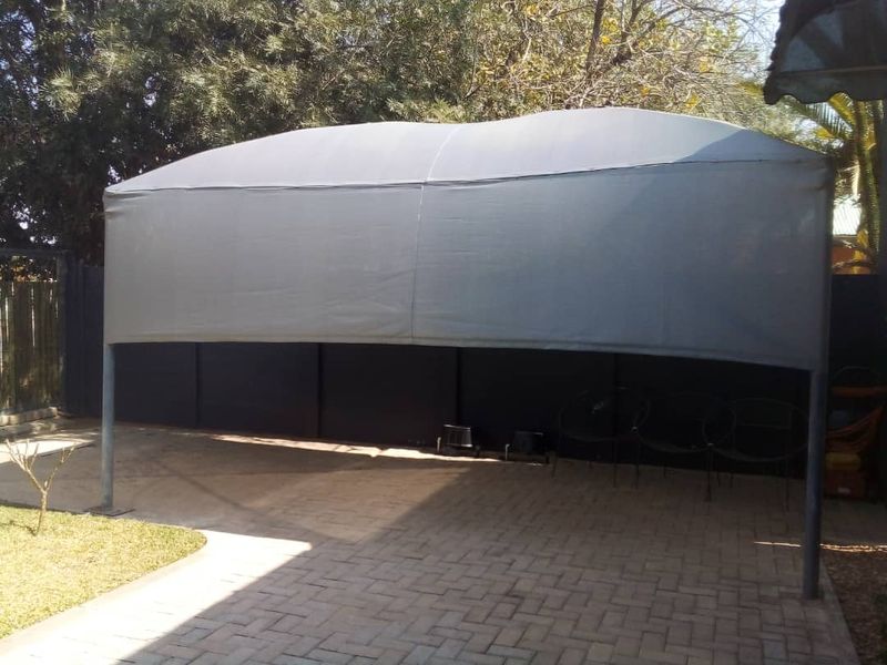 A paved outdoor area featuring a grey shade cloth carport structure, providing covered parking space within a fenced rear yard setting.