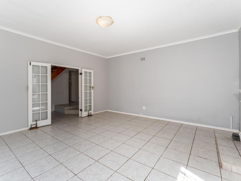 A spacious, empty living room featuring neutral tiled flooring, a fireplace mantel, and classic french doors leading to an adjacent area.
