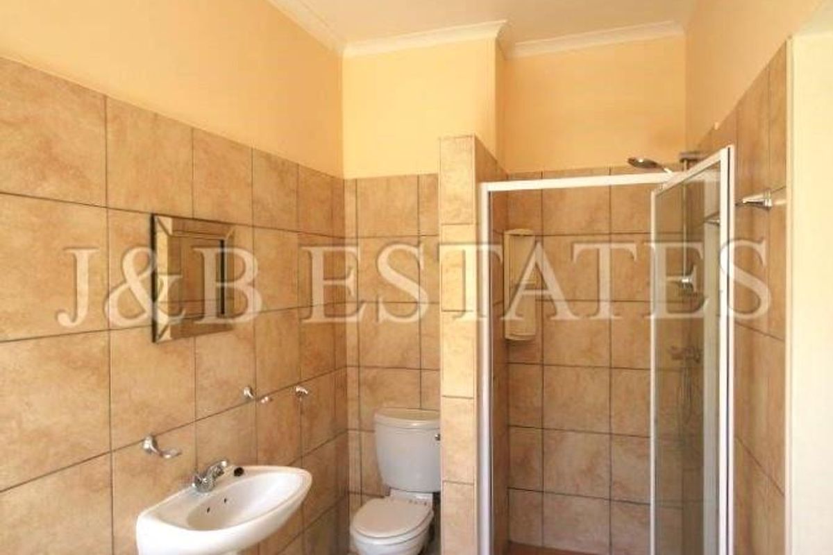 A functional bathroom featuring a shower enclosure, wall-mounted basin, and toilet with neutral floor-to-ceiling tiling.