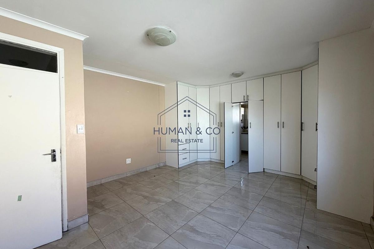 A spacious, empty bedroom featuring neutral wall tones, tiled flooring, and extensive built-in cupboard storage.