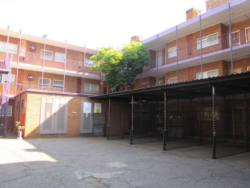 Exterior view of an apartment complex featuring a brick facade, covered parking bays, and communal balcony access.