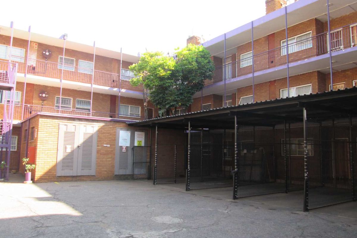 Exterior view of an apartment complex featuring a brick facade, covered parking bays, and communal balcony access.