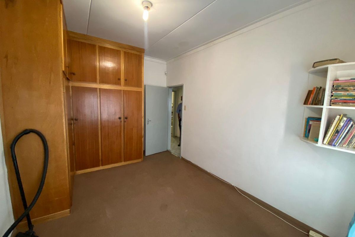 A bedroom featuring built-in wooden cupboards and carpeted flooring, offering a functional space with potential for modernization.