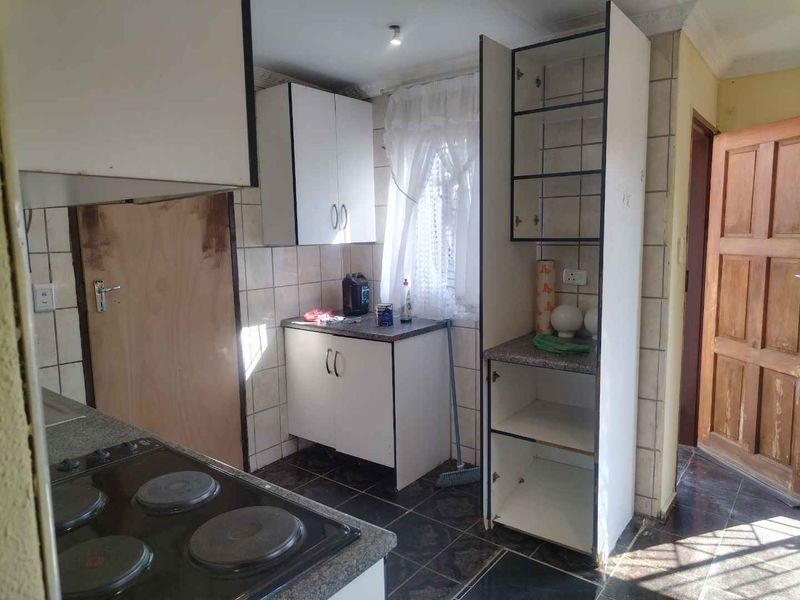 A functional kitchen featuring built-in cabinetry, laminate countertops, and an electric hob, with ceramic tiling throughout the floor and walls.