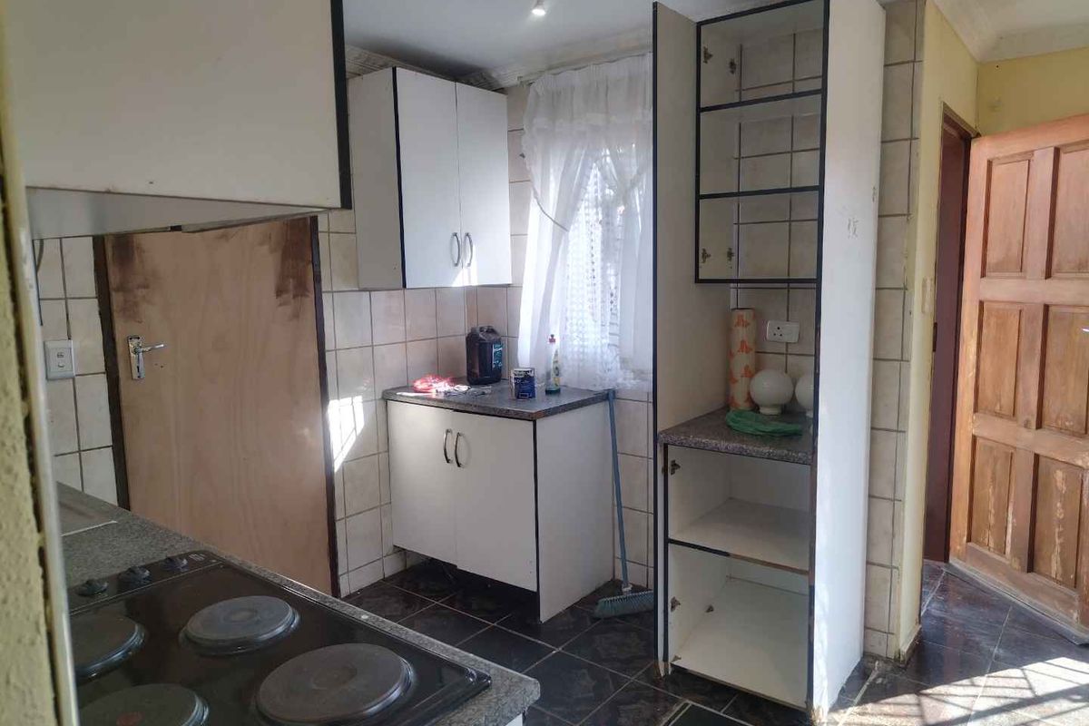 A functional kitchen featuring built-in cabinetry, laminate countertops, and an electric hob, with ceramic tiling throughout the floor and walls.
