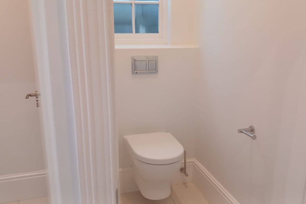 A clean, modern guest bathroom featuring a wall-mounted toilet with a dual-flush plate and neutral finishes.