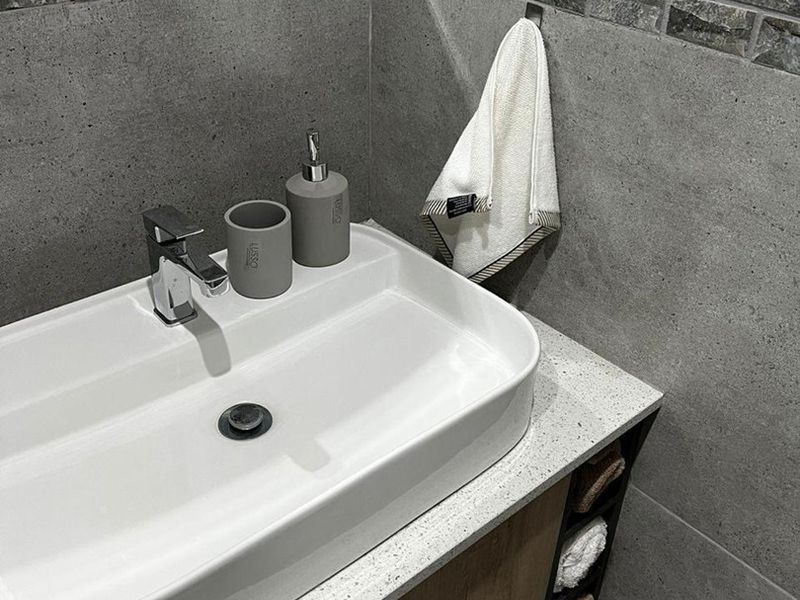 Modern bathroom vanity featuring a white vessel sink, chrome mixer tap, stone countertop, and wood-finish cabinetry with integrated storage.