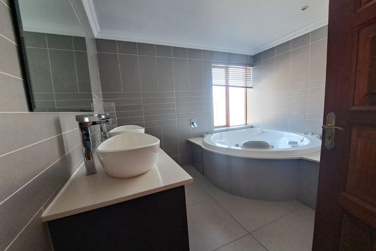 Modern bathroom featuring a built-in vanity with dual vessel sinks, chrome fixtures, and a spacious corner jetted tub with neutral tiled finishes.
