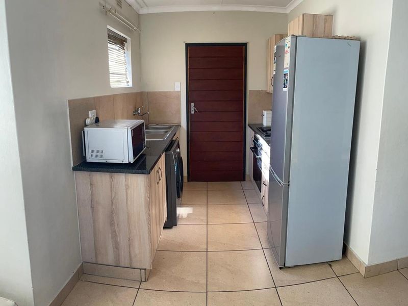 A functional galley-style kitchen featuring laminate cabinetry, granite countertops, tiled flooring, and integrated cooking appliances.