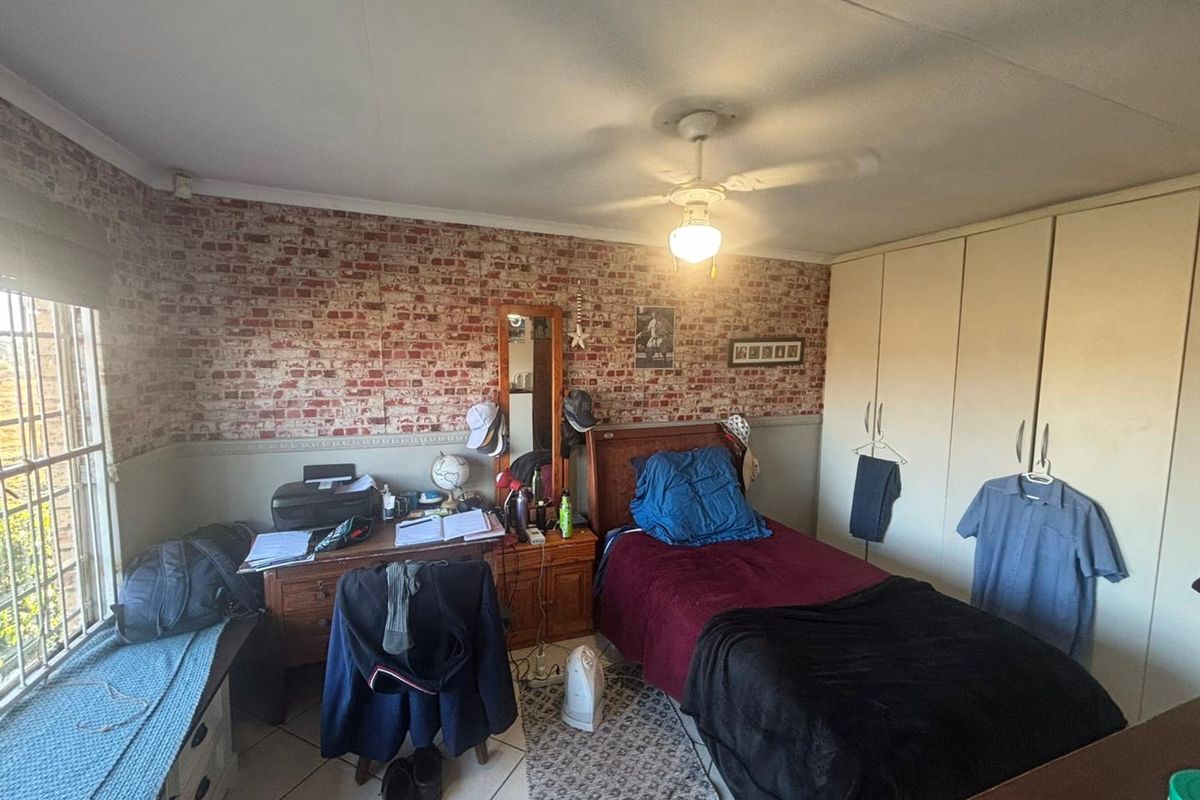 A bedroom featuring built-in cupboards, tiled flooring, and a brick-patterned feature wall, offering a functional space with natural light from the window.