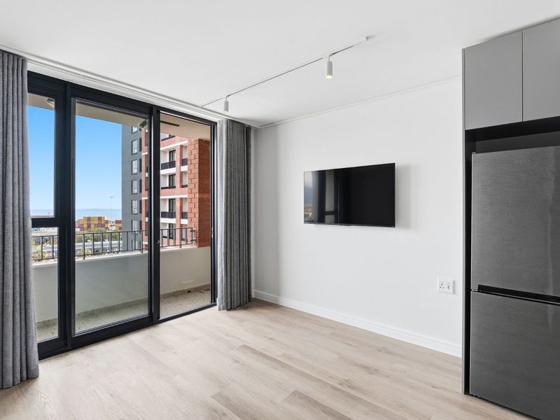 Modern living area featuring light laminate flooring, track lighting, and large sliding glass doors opening to a balcony with urban views.