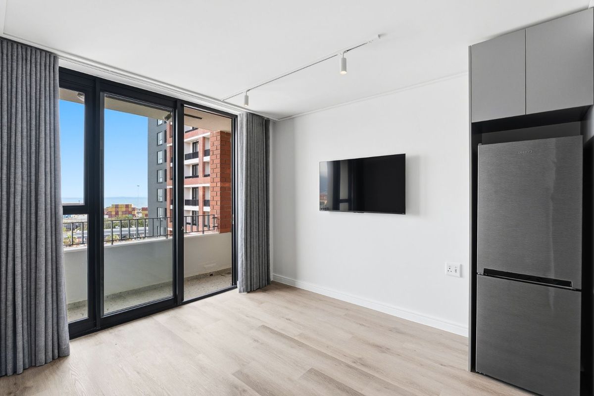 Modern living area featuring light laminate flooring, track lighting, and large sliding glass doors opening to a balcony with urban views.