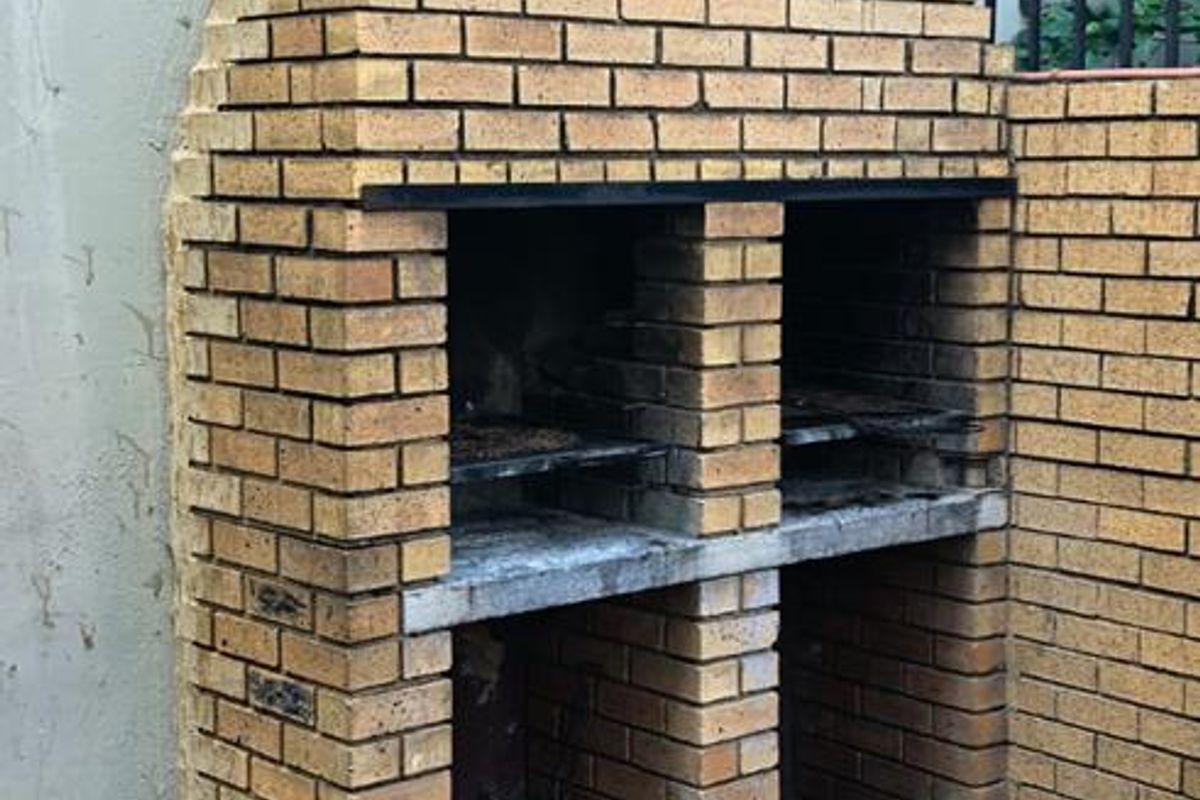 Outdoor area featuring a traditional built-in brick braai and chimney, set against a boundary wall with paved flooring.