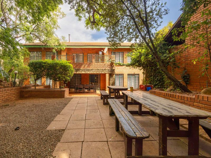 A spacious rear garden featuring a paved patio area, brick retaining walls, and a two-story brick house with a balcony.