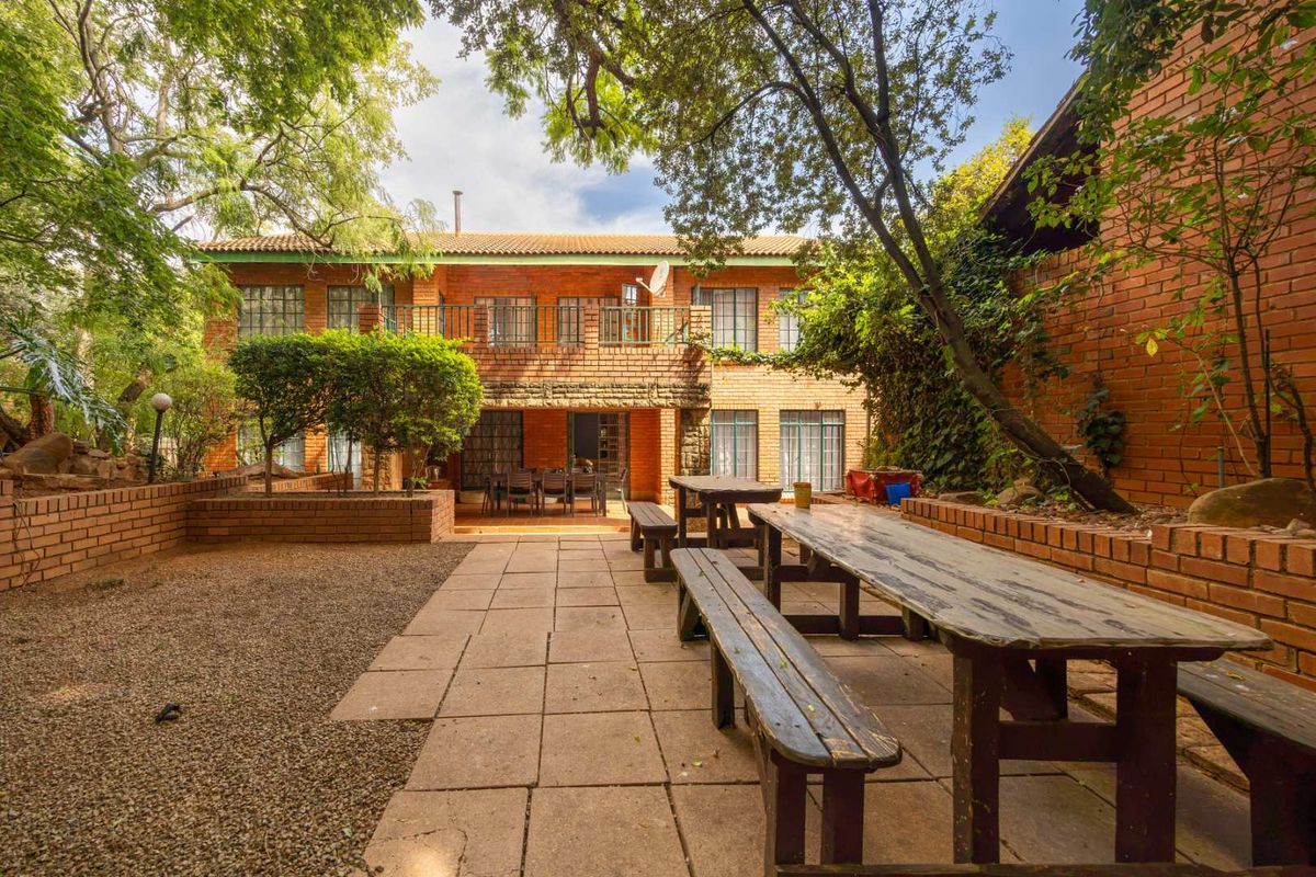 A spacious rear garden featuring a paved patio area, brick retaining walls, and a two-story brick house with a balcony.