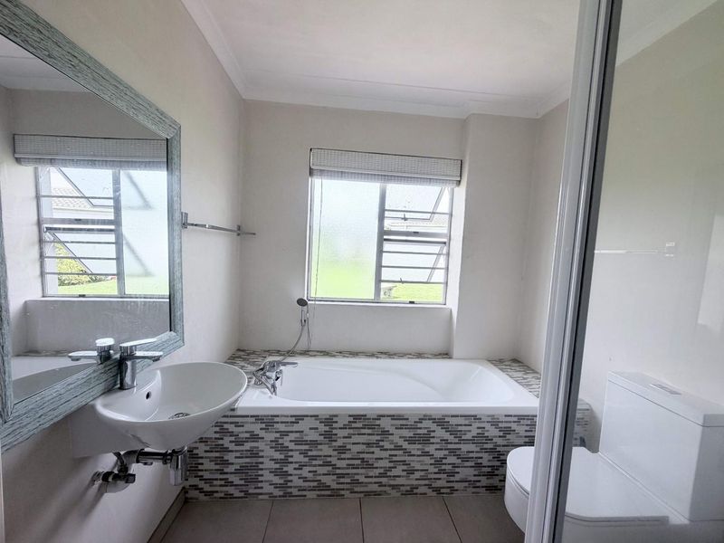 A clean and functional bathroom featuring a built-in bathtub with mosaic tile detailing, a wall-mounted basin, and a toilet.