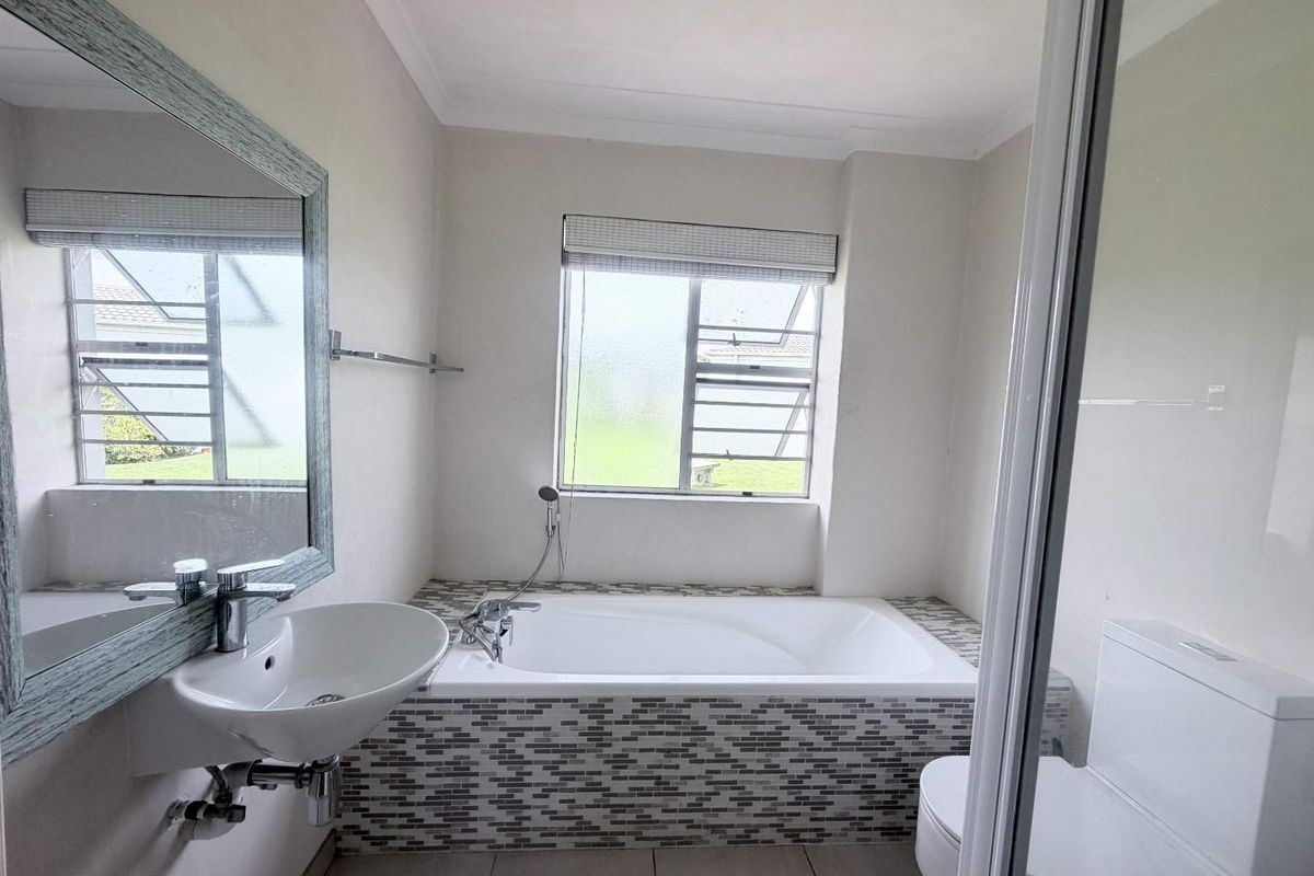 A clean and functional bathroom featuring a built-in bathtub with mosaic tile detailing, a wall-mounted basin, and a toilet.