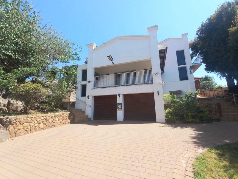 Front elevation of a multi-story house featuring a double garage, paved driveway, stone retaining wall, and an upper-level balcony.