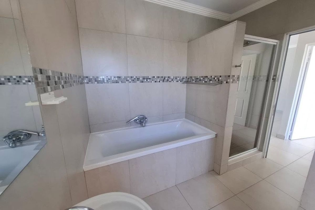 Modern bathroom featuring a built-in bathtub, separate glass-enclosed shower, and neutral wall tiling with a decorative mosaic accent strip.