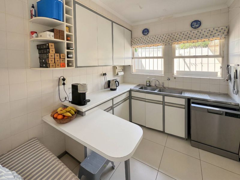 A functional kitchen featuring white cabinetry, tiled splashbacks, double sink, and tiled flooring with a small integrated breakfast nook.