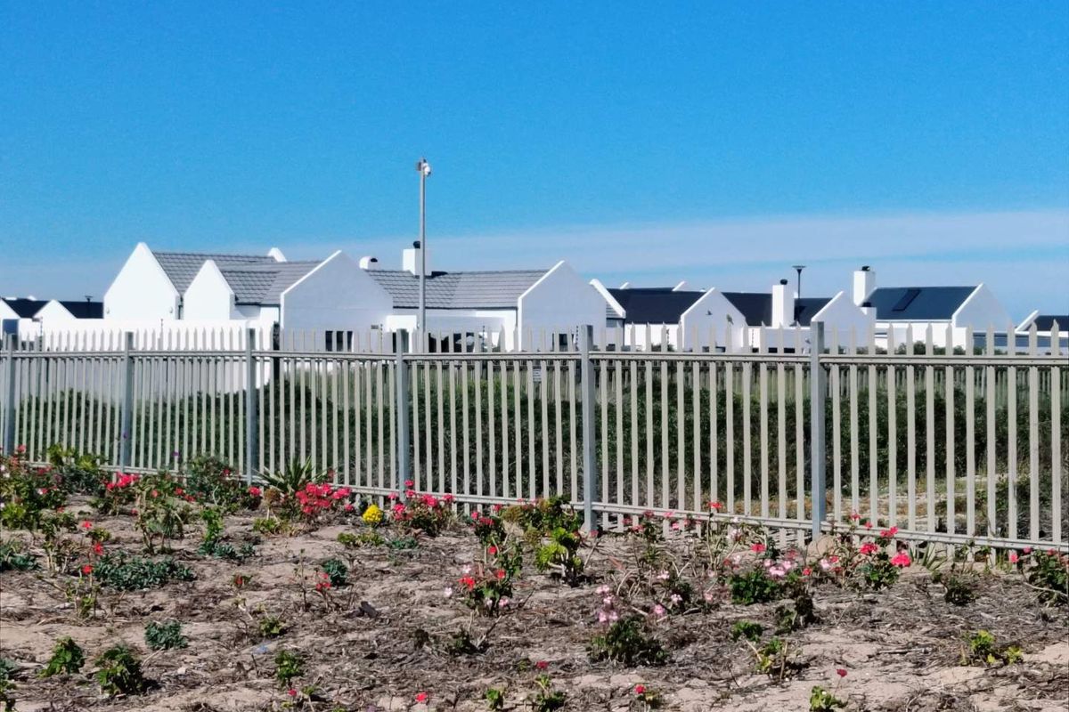 A view of the rear exterior of a residential property featuring white facades, pitched roofs, and secure metal perimeter fencing.