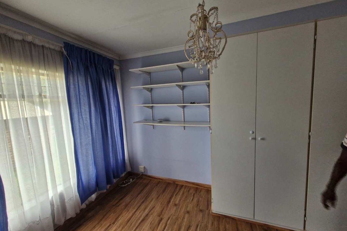 A bedroom featuring built-in wardrobes, wall-mounted shelving, and wood-look laminate flooring.