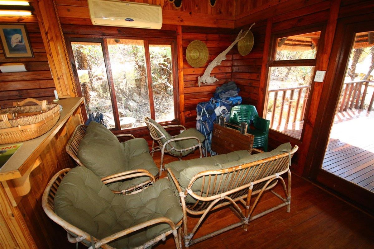 A rustic living area featuring warm timber wall cladding, polished timber flooring, and large sliding doors that open onto an outdoor timber deck.