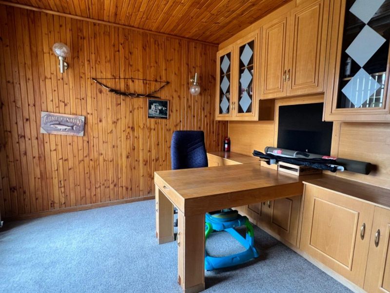 A home office featuring extensive built-in wooden cabinetry, integrated desk space, and traditional timber wall and ceiling paneling.