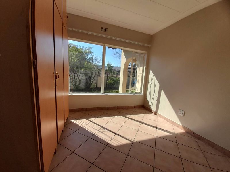 A bright, empty bedroom featuring tiled flooring and built-in wooden cupboards, offering a clean canvas with natural light.