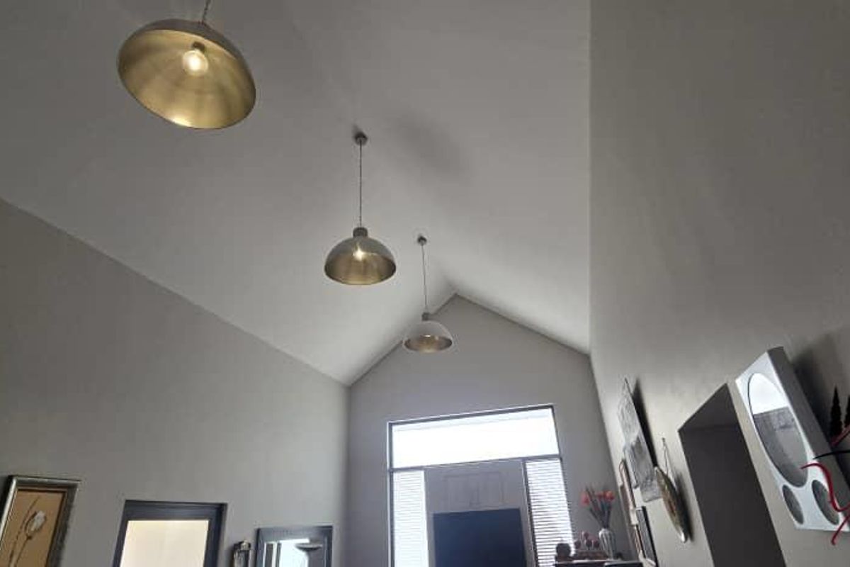 A spacious living area featuring a high vaulted ceiling with modern pendant lighting and large windows allowing for ample natural light.