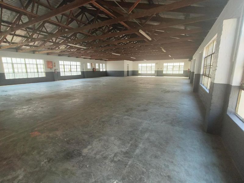 Spacious industrial utility area featuring exposed timber roof trusses, concrete flooring, and large steel-framed windows providing ample natural light.