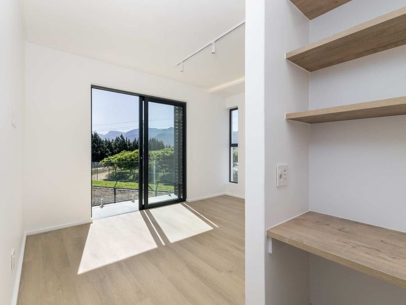 A bright, modern bedroom featuring light wood-look flooring, built-in shelving and desk space, and a sliding glass door with scenic mountain views.