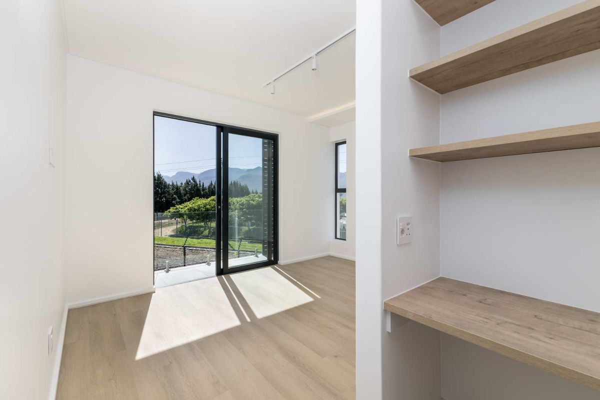 A bright, modern bedroom featuring light wood-look flooring, built-in shelving and desk space, and a sliding glass door with scenic mountain views.