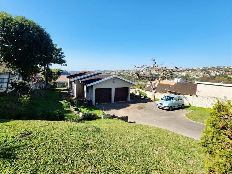 Front view of a residential property featuring a double garage, paved driveway, and surrounding garden area with established trees.