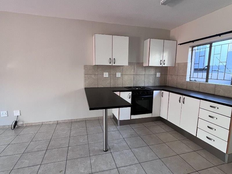 A functional, empty kitchen featuring white cabinetry, dark countertops, built-in oven and hob, and tiled flooring with a neutral wall finish.