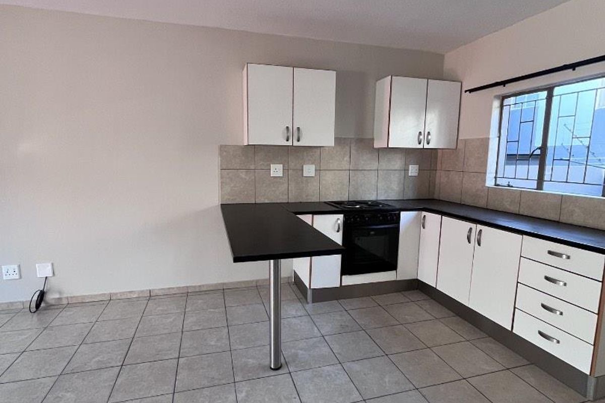 A functional, empty kitchen featuring white cabinetry, dark countertops, built-in oven and hob, and tiled flooring with a neutral wall finish.