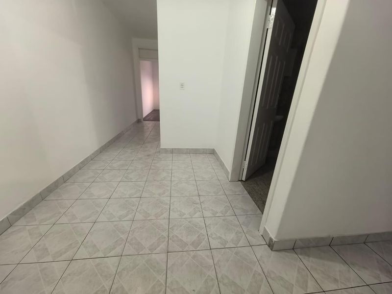 A clean, empty hallway featuring neutral ceramic floor tiles and white walls, providing access to adjacent rooms.