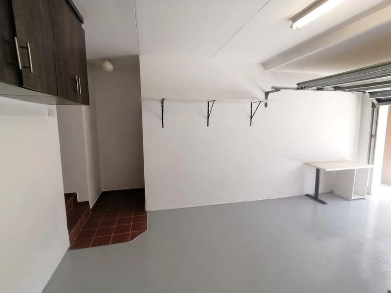 A clean and spacious garage featuring painted concrete flooring, built-in wall shelving, and direct internal access via a tiled step area.
