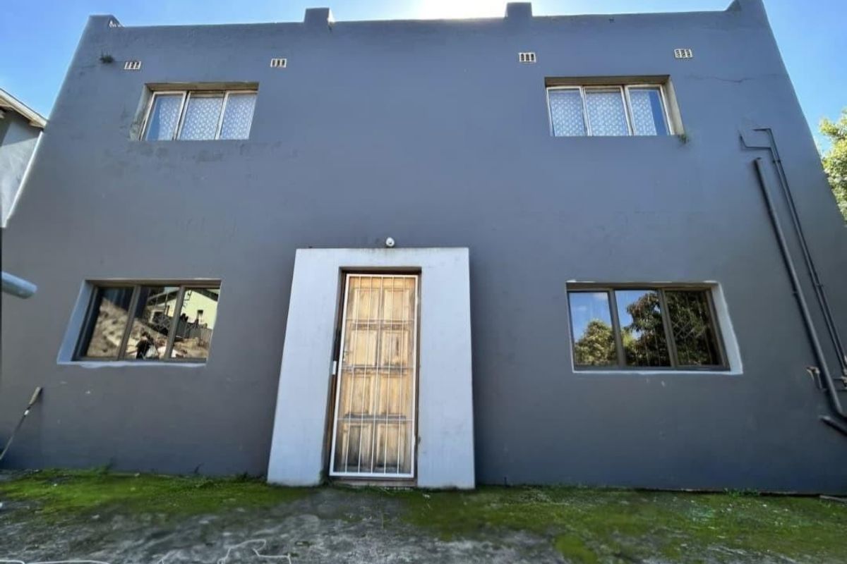 Rear elevation of a two-story house featuring grey painted exterior walls, aluminium window frames, and a security gate entrance.