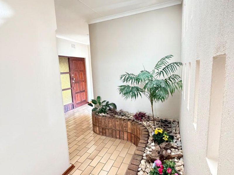A bright, spacious hallway featuring a skylight, tiled flooring, and a built-in brick planter box with decorative wall niches.