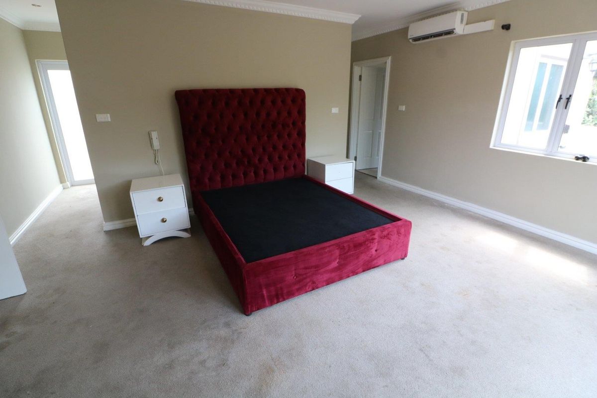 Spacious bedroom featuring neutral wall tones, carpeted flooring, cornice detailing, and a wall-mounted air conditioning unit.