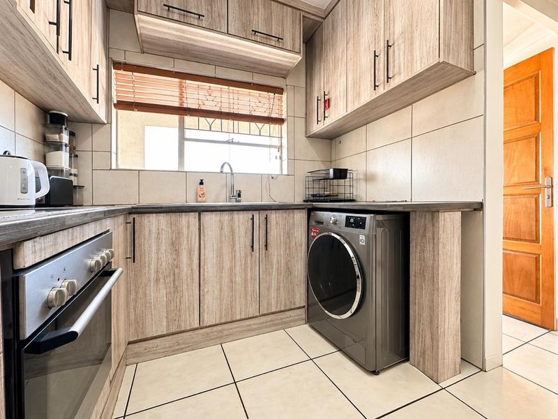 Modern kitchen featuring light wood-grain cabinetry, dark laminate countertops, tiled backsplash, built-in oven, and integrated space for a washing machine.