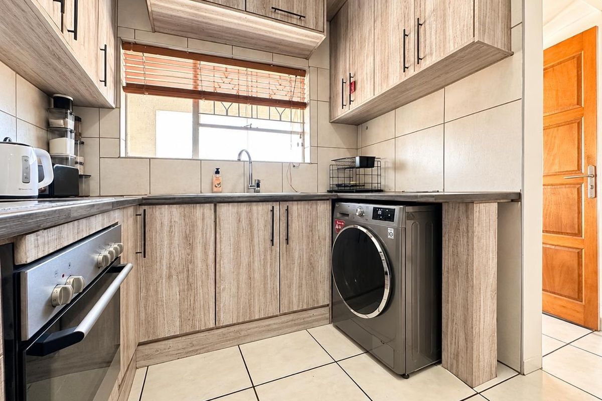 Modern kitchen featuring light wood-grain cabinetry, dark laminate countertops, tiled backsplash, built-in oven, and integrated space for a washing machine.