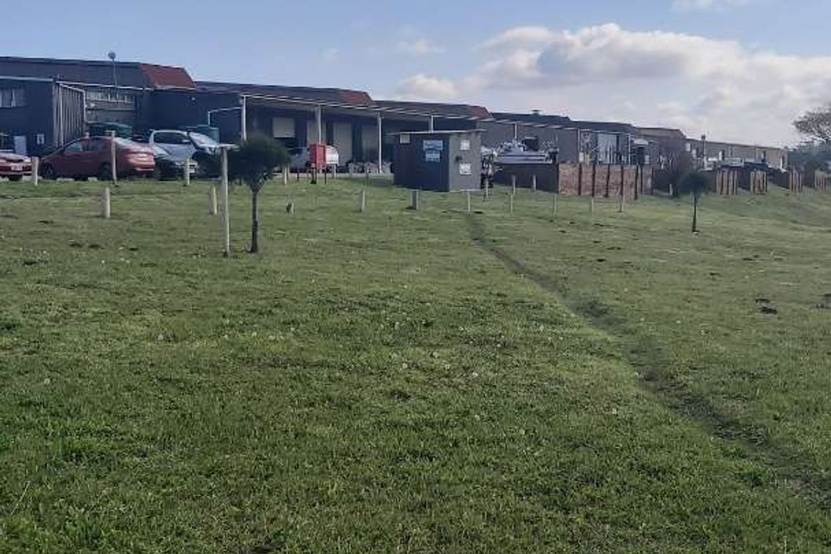 Exterior view of an industrial complex featuring a row of units with paved parking areas and a large grassed foreground.