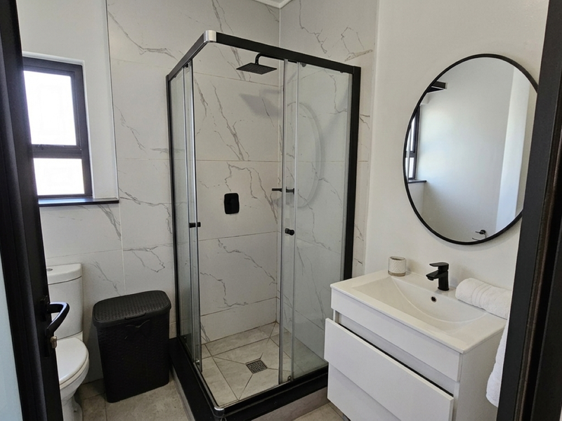 Modern bathroom featuring a glass shower enclosure with a rain shower head, a sleek vanity with basin, and elegant marble-look wall tiling.