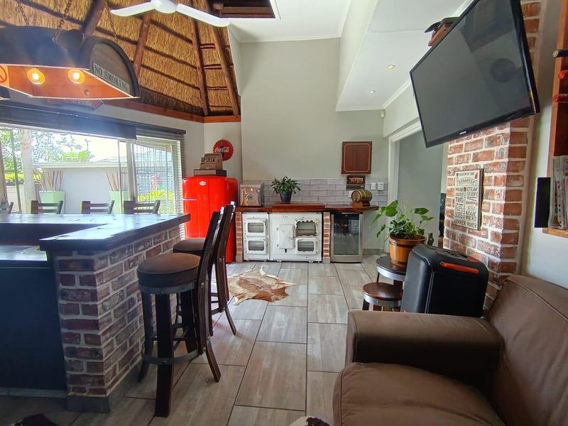 A rustic-style bar area featuring a brick counter, thatched ceiling, tiled floors, and built-in cooking appliances, opening out to the garden through sliding doors.
