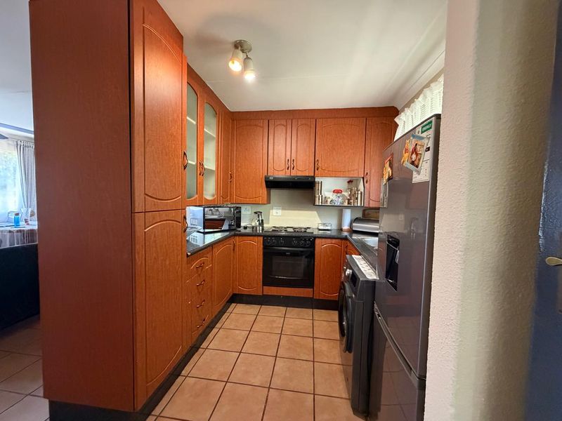 A functional kitchen featuring wood-finish cabinetry, built-in oven and hob, extractor fan, and tiled flooring.