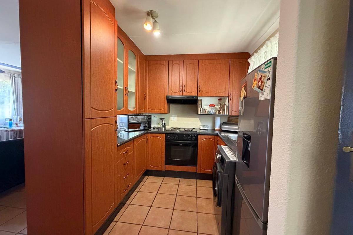 A functional kitchen featuring wood-finish cabinetry, built-in oven and hob, extractor fan, and tiled flooring.